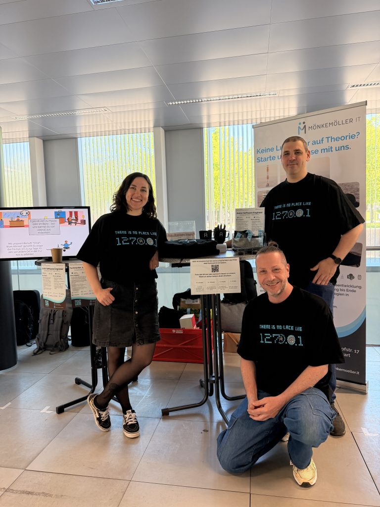 Julia, Fabian und Markus vor dem Messestand der Recruitingmesse im April. Im Hintergrund sieht man einen Bildschirm mit einem Video der Firma.